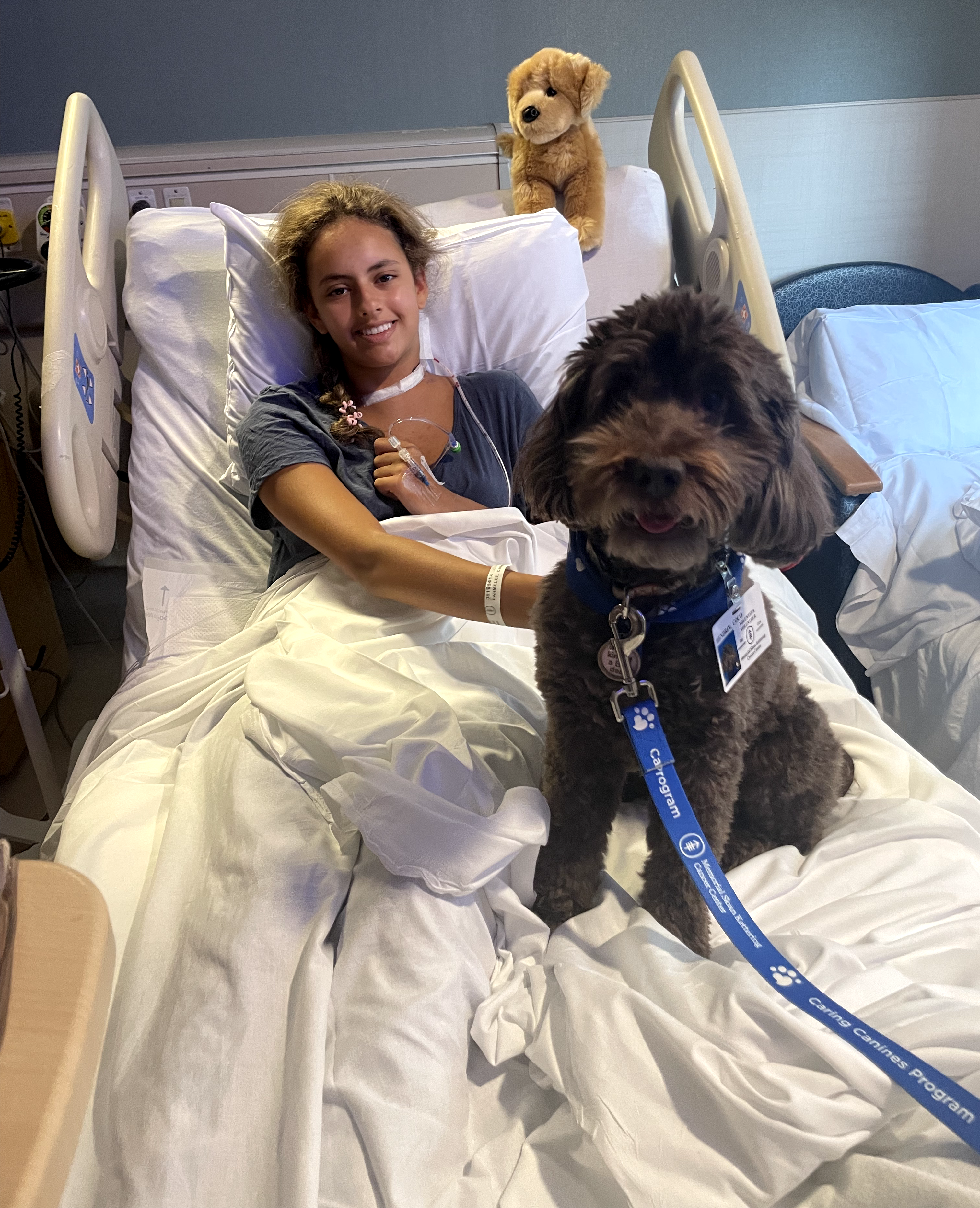 Cami Parmelee in a hospital bed with a therapy dog during her cancer treatment